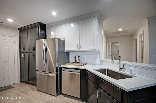 kitchen featuring appliances with stainless steel finishes, light wood-type flooring, backsplash, sink, and white cabinets