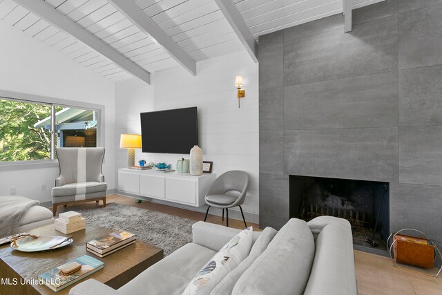 living room featuring vaulted ceiling with beams, light hardwood / wood-style flooring, and a tile fireplace