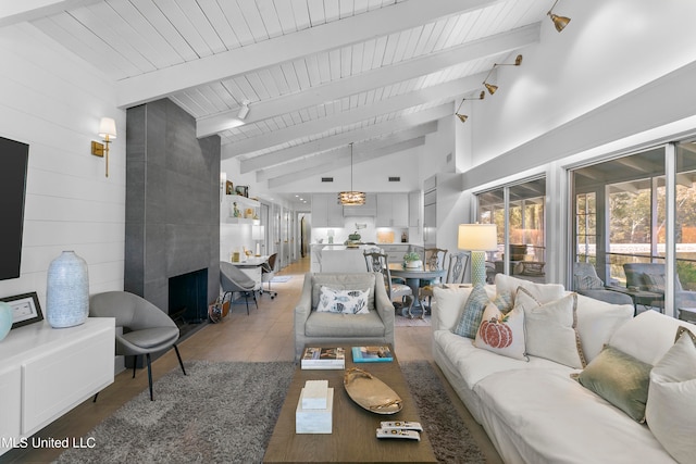 living room featuring vaulted ceiling with beams, track lighting, a large fireplace, and wooden walls