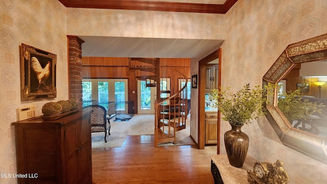 hallway featuring french doors, light hardwood / wood-style floors, wood walls, and crown molding