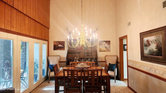 dining space featuring wood walls, a towering ceiling, and an inviting chandelier