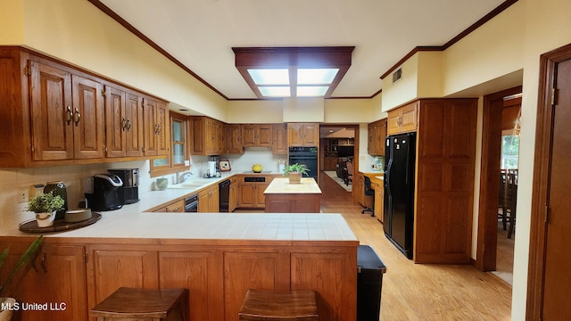 kitchen with kitchen peninsula, backsplash, light hardwood / wood-style flooring, black appliances, and sink