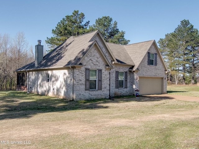 view of front of house with driveway, a chimney, a front yard, an attached garage, and brick siding