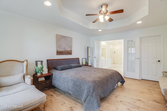 bedroom with light wood finished floors, a tray ceiling, recessed lighting, ornamental molding, and connected bathroom