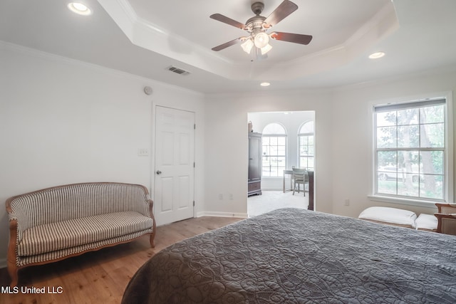 bedroom with a raised ceiling, multiple windows, visible vents, and ornamental molding