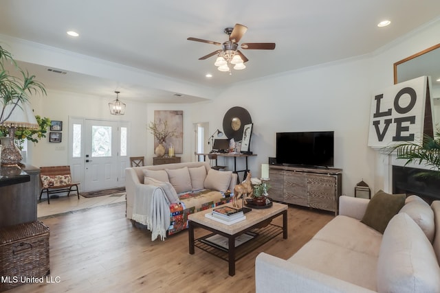 living area with visible vents, light wood-style flooring, ornamental molding, ceiling fan with notable chandelier, and recessed lighting