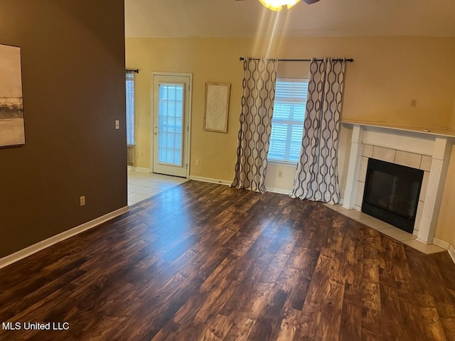 unfurnished living room with a tiled fireplace, wood-type flooring, and ceiling fan