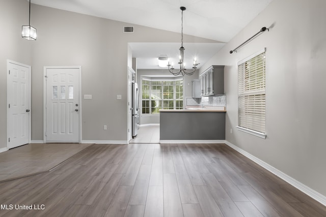 kitchen featuring a chandelier, gray cabinetry, freestanding refrigerator, wood finished floors, and high vaulted ceiling