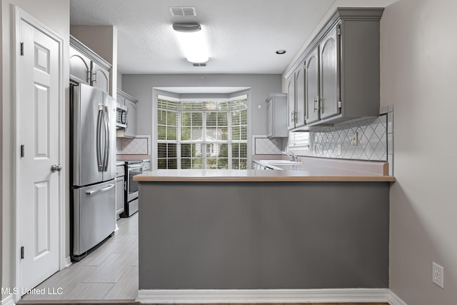 kitchen featuring appliances with stainless steel finishes, gray cabinets, a sink, a peninsula, and decorative backsplash