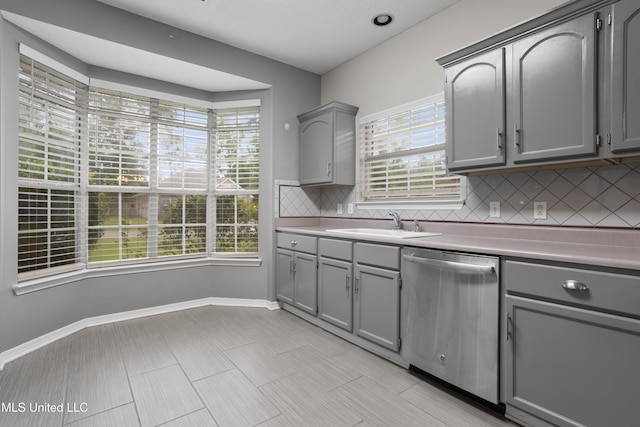 kitchen featuring stainless steel dishwasher, gray cabinets, tasteful backsplash, light countertops, and a sink