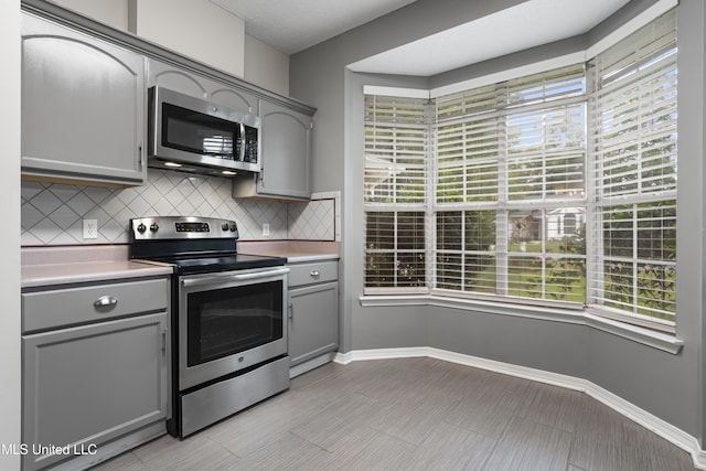 kitchen with stainless steel appliances, gray cabinets, backsplash, and baseboards