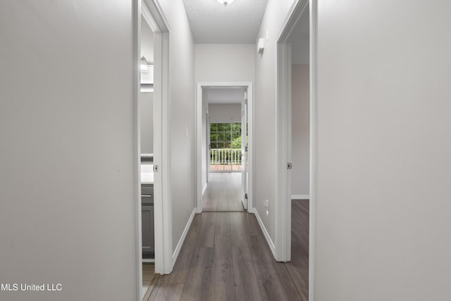 hall featuring baseboards, wood finished floors, and a textured ceiling