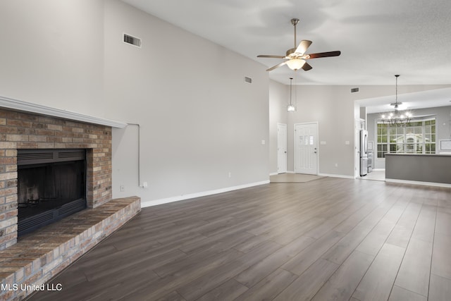 unfurnished living room with ceiling fan, a fireplace, wood finished floors, high vaulted ceiling, and a chandelier