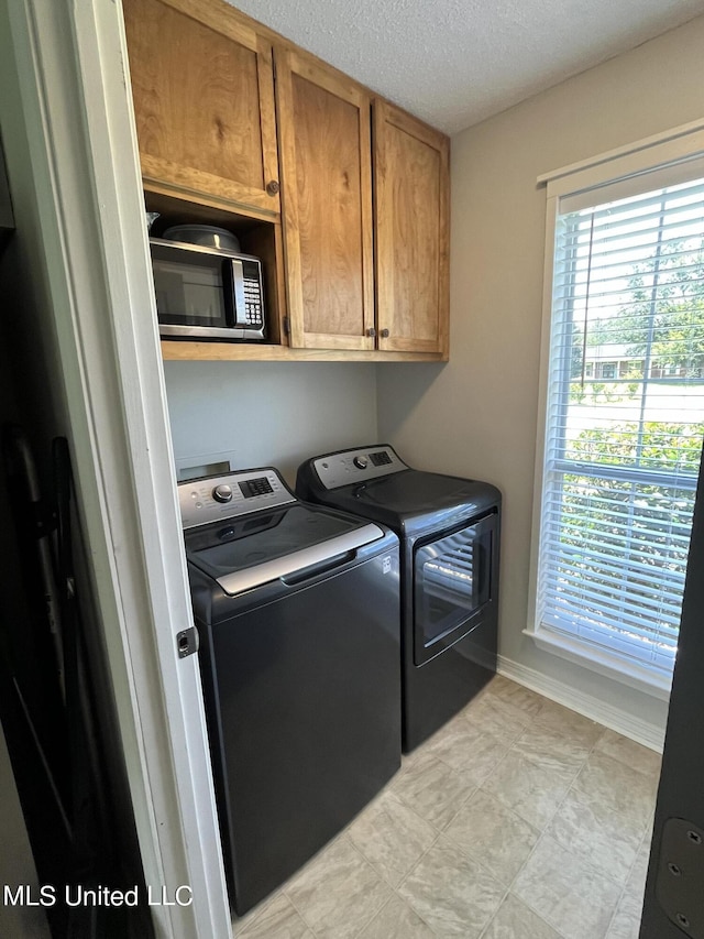 laundry room featuring a wealth of natural light, independent washer and dryer, a textured ceiling, and cabinet space