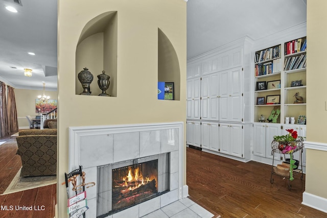 living room featuring a tile fireplace, hardwood / wood-style flooring, built in features, ornamental molding, and a chandelier