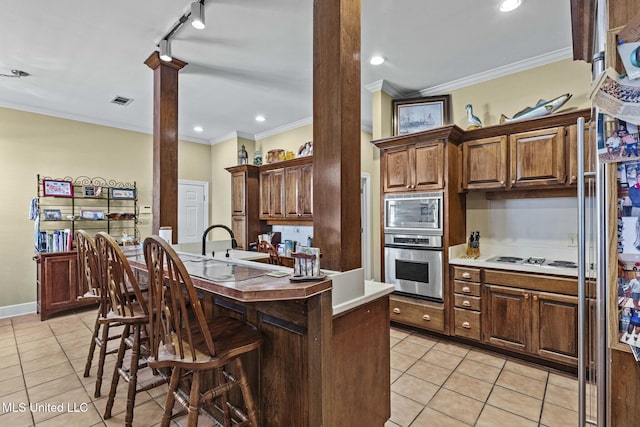 kitchen featuring crown molding, a kitchen bar, a kitchen island with sink, light tile patterned floors, and appliances with stainless steel finishes