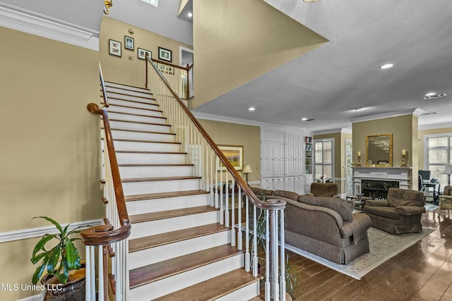 stairway featuring crown molding, a high end fireplace, and wood-type flooring