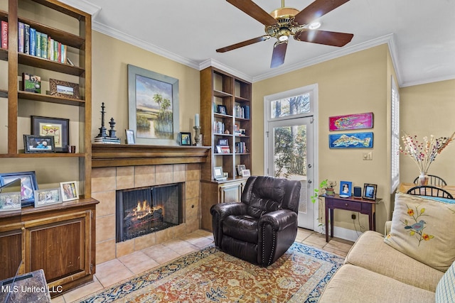 sitting room featuring a tiled fireplace, ceiling fan, light tile patterned floors, and ornamental molding