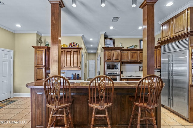 kitchen featuring a kitchen bar, ornamental molding, built in appliances, a center island, and light tile patterned flooring