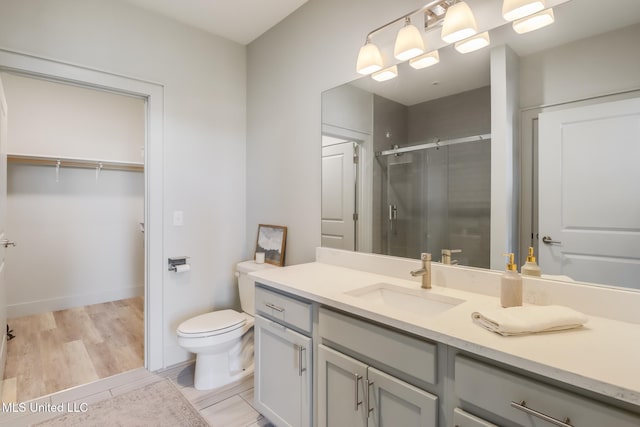 bathroom featuring a spacious closet, toilet, a stall shower, vanity, and wood finished floors