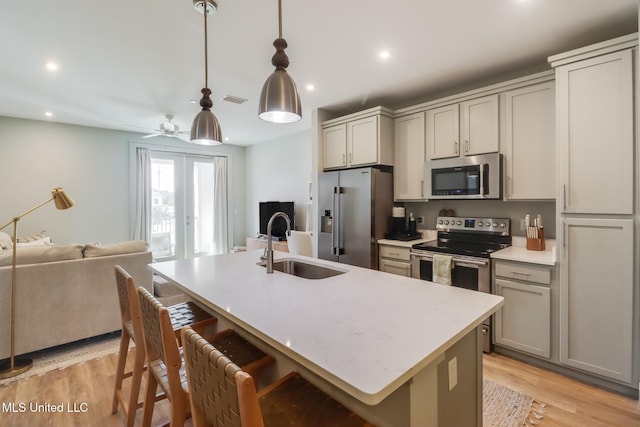 kitchen featuring french doors, light wood finished floors, appliances with stainless steel finishes, open floor plan, and a sink