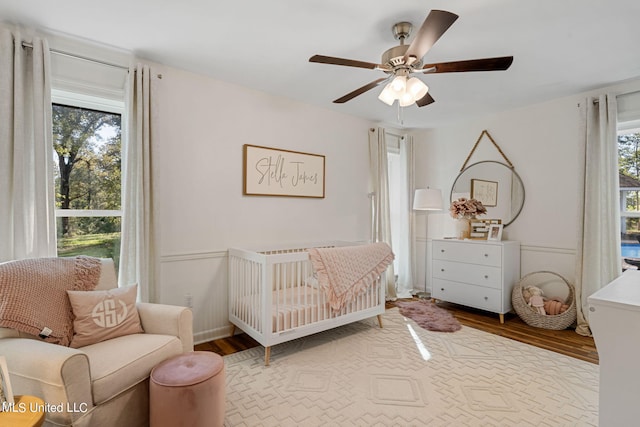 bedroom with ceiling fan, hardwood / wood-style floors, and a crib