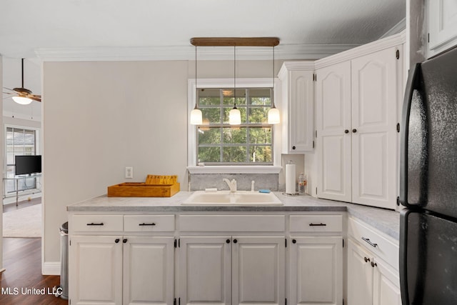 kitchen featuring white cabinets, decorative light fixtures, black refrigerator, and a wealth of natural light