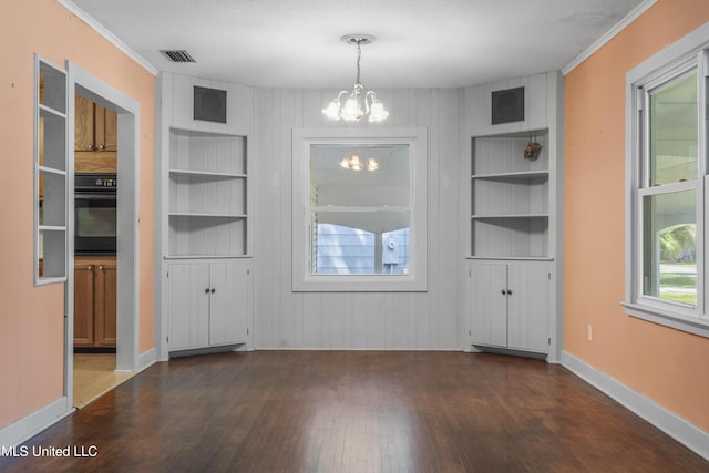 unfurnished dining area with visible vents, crown molding, built in shelves, wood finished floors, and an inviting chandelier