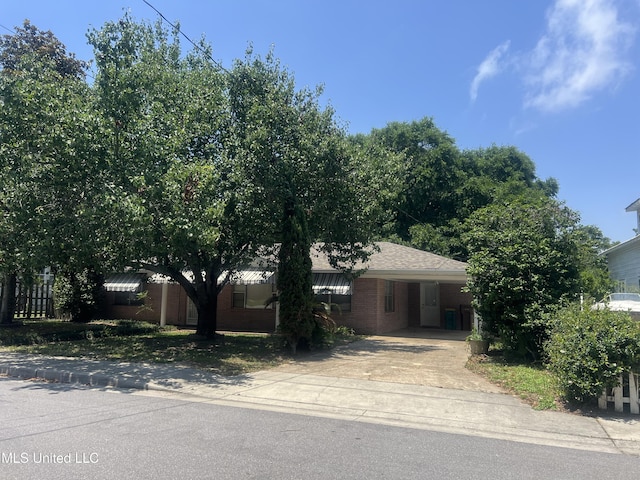 241 Iroquois St, Biloxi, MS 39530 - view of property hidden behind natural elements featuring concrete driveway, an attached carport, and brick siding
