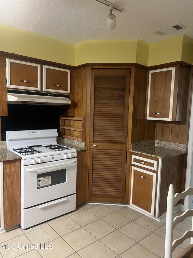 241 Iroquois St, Biloxi, MS 39530 - kitchen with white range with gas stovetop, under cabinet range hood, a textured ceiling, light tile patterned floors, and stone counters