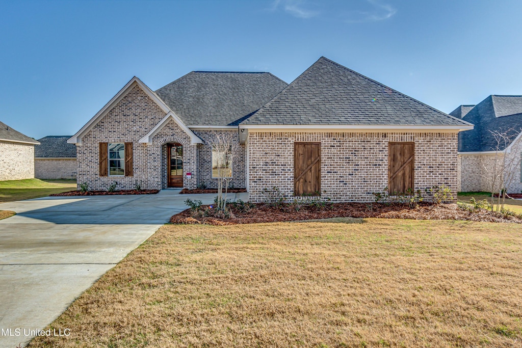 view of front of property with a shingled roof, a front lawn, and brick siding