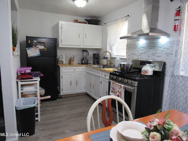 kitchen featuring stainless steel gas range, ventilation hood, white cabinetry, and black fridge