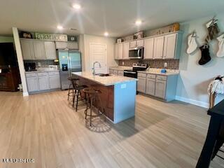 154 Magnolia Farms Dr, Lucedale, MS 39452 - kitchen featuring stainless steel appliances, a breakfast bar area, a sink, light wood-style flooring, and tasteful backsplash