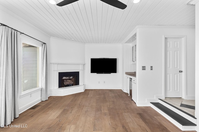 unfurnished living room with ornamental molding, wood ceiling, a brick fireplace, and wood-type flooring