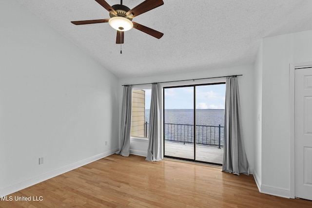 spare room with a textured ceiling, light wood-type flooring, ceiling fan, and a water view