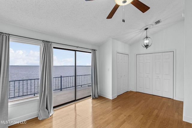 unfurnished bedroom with access to outside, light wood-type flooring, a textured ceiling, and a water view