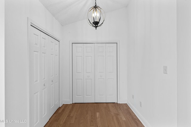 corridor with wood-type flooring, a textured ceiling, and a notable chandelier