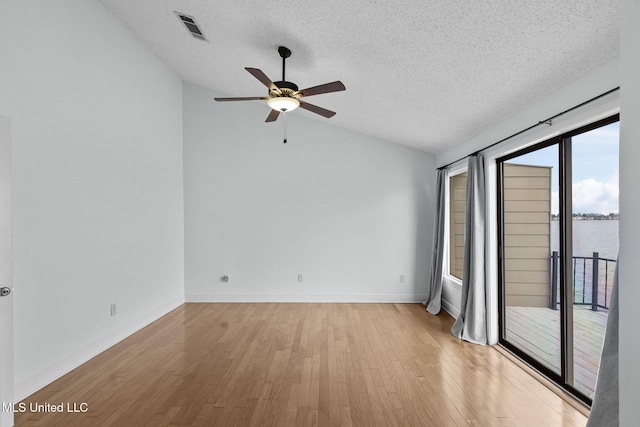 unfurnished room featuring vaulted ceiling, a textured ceiling, light hardwood / wood-style floors, and a water view