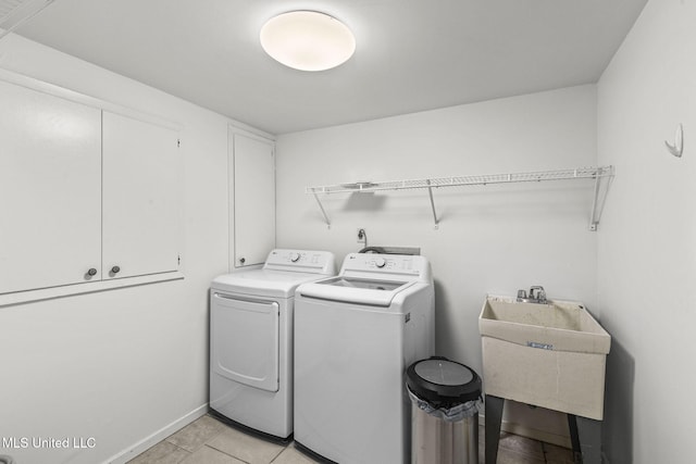 clothes washing area with sink, washer and clothes dryer, light tile patterned floors, and cabinets