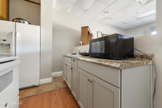 kitchen featuring a paneled ceiling, white refrigerator with ice dispenser, stove, light stone countertops, and light wood-type flooring