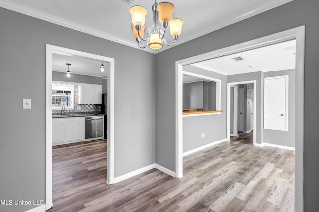 unfurnished dining area with baseboards, visible vents, ornamental molding, wood finished floors, and a chandelier