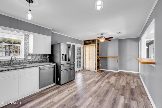 kitchen featuring stainless steel appliances, a sink, white cabinets, dark stone counters, and crown molding