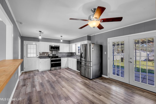 kitchen featuring wood finished floors, white cabinetry, ornamental molding, french doors, and appliances with stainless steel finishes