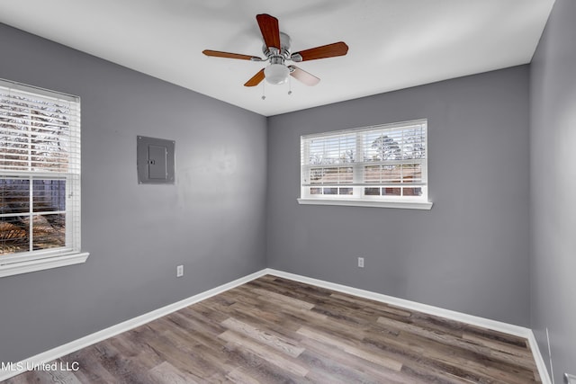 spare room featuring a ceiling fan, wood finished floors, electric panel, and baseboards