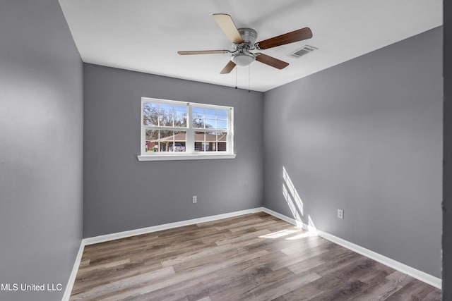 empty room featuring a ceiling fan, baseboards, visible vents, and wood finished floors