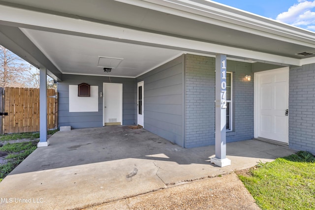 doorway to property with brick siding, fence, and visible vents