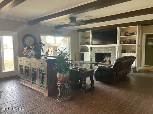 living room featuring beam ceiling, a stone fireplace, a wealth of natural light, and ornamental molding