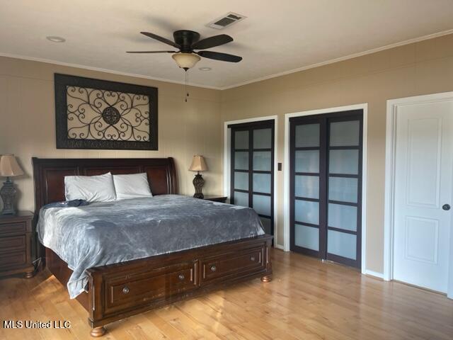 bedroom featuring ceiling fan, crown molding, two closets, and light wood-type flooring