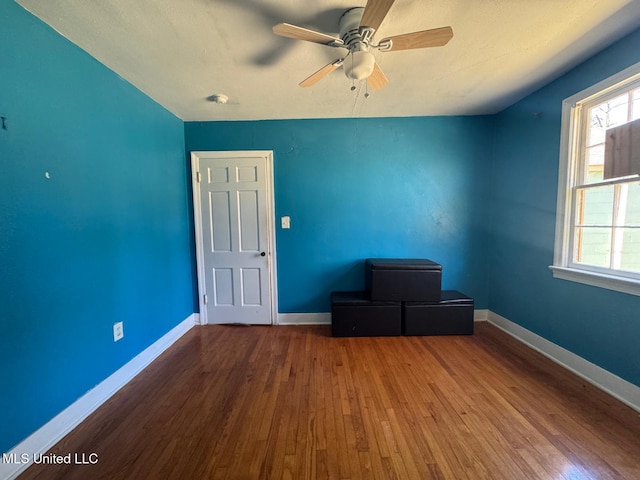 empty room with wood finished floors, a ceiling fan, and baseboards