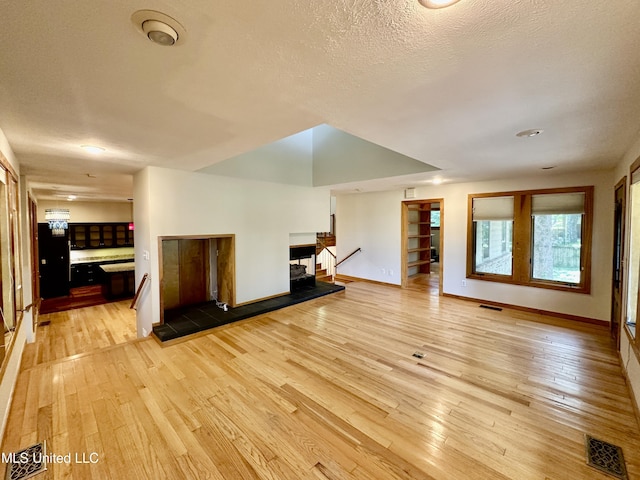 211 Monterey Dr, Clinton, MS 39056 - unfurnished living room with light wood-style floors, baseboards, a fireplace with raised hearth, and a textured ceiling